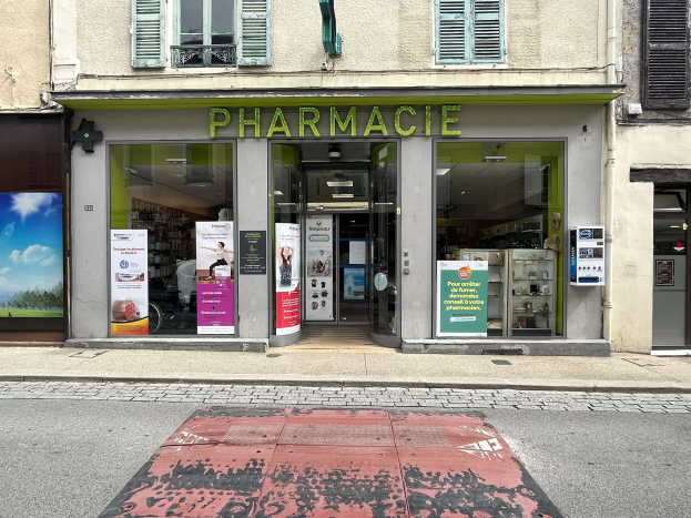 Apotheke mit Glasw├Ąnden und -türen, Plakate an den W├Ąnden, an einer Stra├čenkreuzung mit einer sichtbaren Stra├če unten.