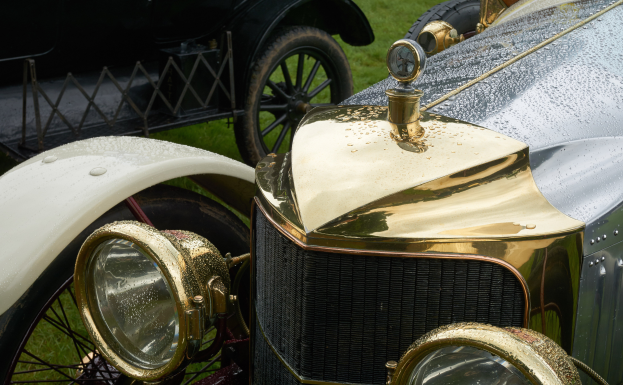 Ein Oldtimer mit Vorderrad, der auf einem grasigen Feld neben einem anderen Auto geparkt ist.