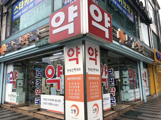 Außenansicht einer modernen Glaswand-Apotheke in Seoul, Südkorea, mit Text, der angibt, dass es sich um die erste Apotheke der Stadt handelt.