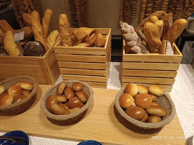 Holztisch mit Körben voller Brot, Tellern und Löffeln in einer Pariser Bäckerei mit einer Wasserzeichenwand.