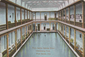 Alte Postkarte des West Baden Springs Hotels mit großem Indoor-Schwimmbad und Menschen, Säulen, Geländern, Stühlen und Text unten.