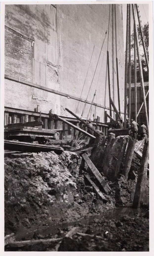 Ein Schwarz-Weiß-Foto einer Baustelle für das New Yorker Staatsgefängnis, das Menschen, hölzerne Gegenstände, Pfähle, Seile, eine Wand und Bäume im Hintergrund zeigt.