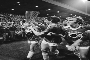 Eine Gruppe von Männern, die einen Pokal auf einem Fußballfeld halten, umgeben von einer Menge hinter einem Zaun, die ihren Sieg im FA Cup Finale feiert, dargestellt in Schwarz-Weiß.
