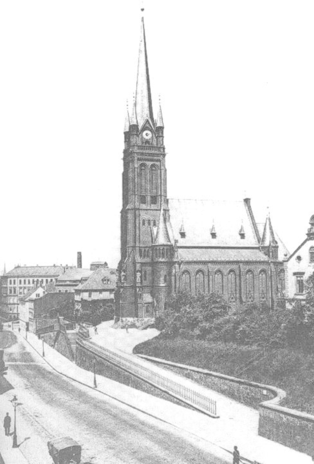Schwarzes und weißes Foto einer Stadtstraße mit der St. Peter Kirche im Hintergrund in Wiesbaden, Deutschland, gesäumt von Gebäuden, Bäumen, Fahrzeugen und einigen Fußgängern.