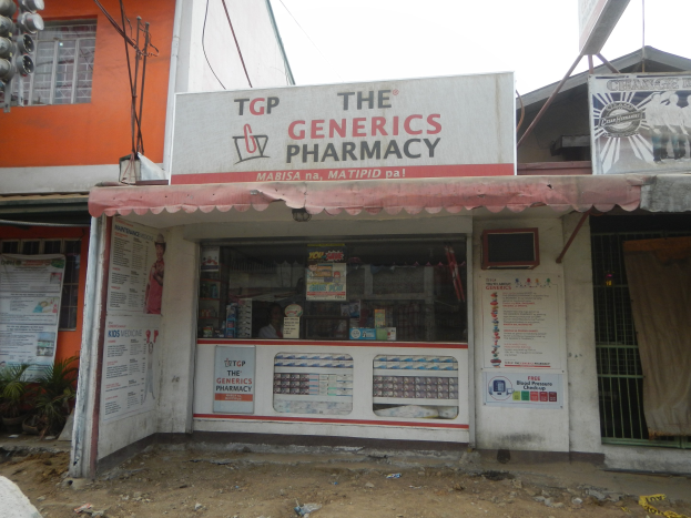 Außenansicht der "Generics Apotheke" mit umliegenden städtischen Elementen unter einem klaren blauen Himmel.