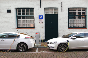 Zwei Elektroautos nebeneinander vor einem weißen Gebäude geparkt, an eine Ladestation angeschlossen.