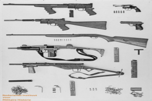 Schwarz-weiß-Foto von verschiedenen Waffen, Munition und Gegenständen, die auf einer Oberfläche verstreut sind, mit Text unten.