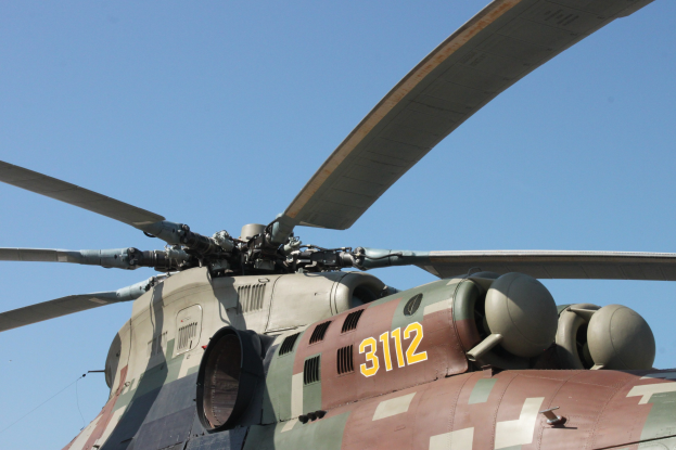 Militärhubschrauber mit Text und Zahlen auf seiner Rumpfseite auf einem Flughafenvorfeld unter einem hellblauen Himmel.