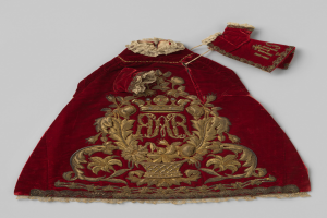 Ein roter Samtmantel mit goldener Stickerei und einer Krone, der gegen einen weißen Hintergrund gestellt ist und detaillierte Designs zeigt.