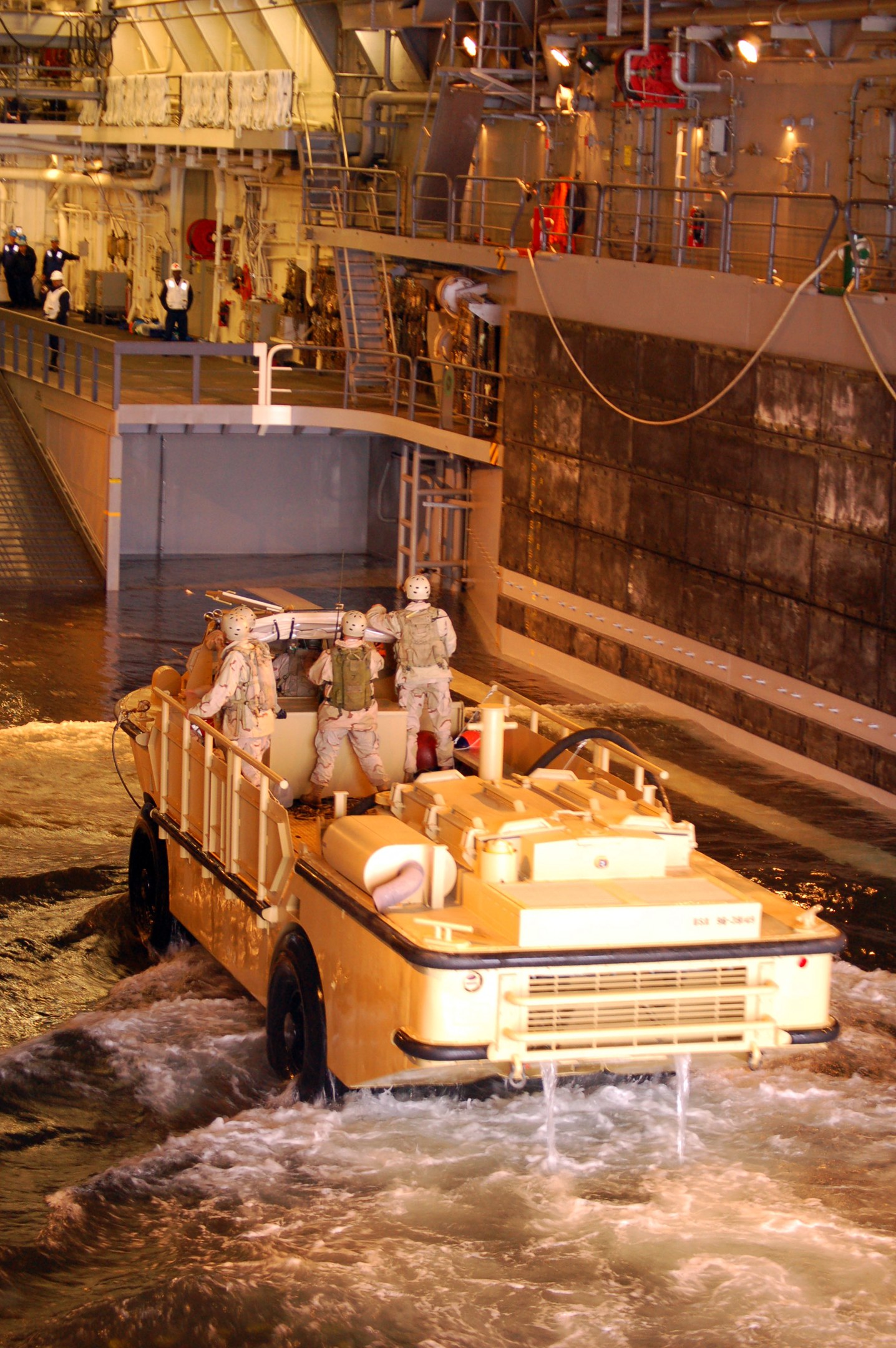 Amphibisches Fahrzeug mit Helmträgern, die durch Wasser fahren, nahe einer Wand, Geländern, Lampen und Rohren im Hintergrund.