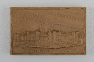 Holztafel an einer Gebäudewand mit der Aufschrift "Centennial Exposition Memorial Hall" und einem eingravierten Bild des Gebäudes.