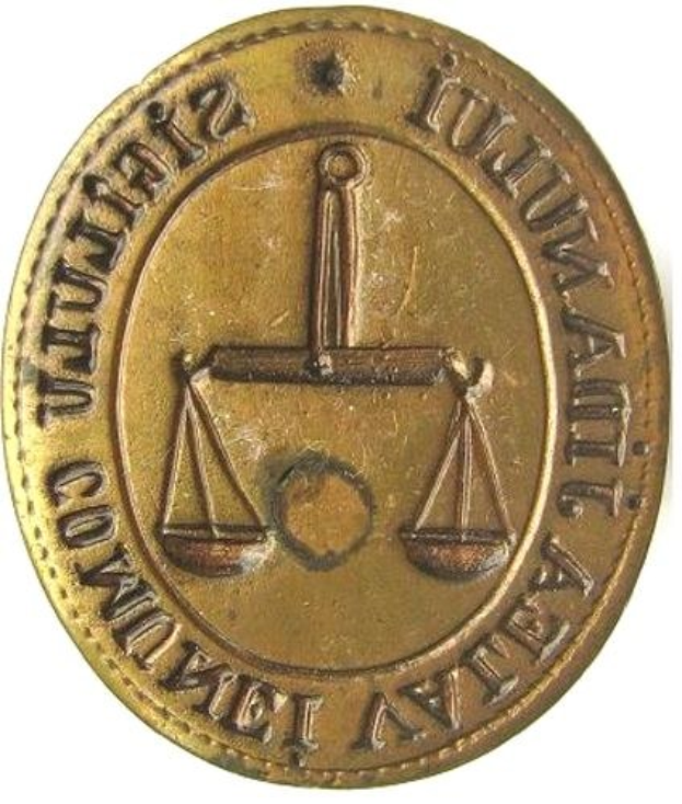 Goldmünze mit Waagschalen-Design und eingravierter Inschrift auf weißem Hintergrund.