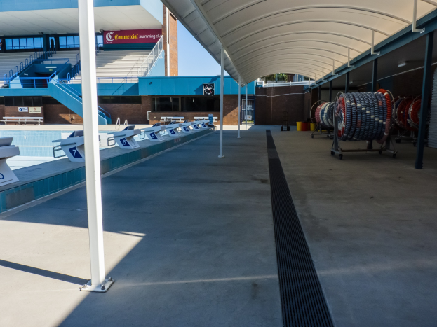 Großes Hallenbad an der Universität von Texas in Austin mit zahlreichen Stühlen, Pfählen, einem Gebäude, Treppen, Geländern und Texttafeln im Hintergrund.