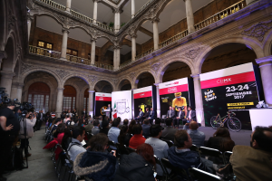 Eine Gruppe von Menschen sitzt an einem Tisch mit einem Podium und einem Mikrofon vor einer Menge, Kameras und Transparenten während einer Pressekonferenz für das CDMX 2017-Event.