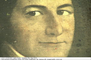 Schwarzes und weißes Porträt einer Frau mit zurückgekämmtem Haar, ernster Miene, direktem Blick und leichtem Lächeln, mit Text unten.