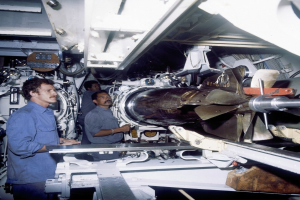 Drei Männer in einer Fabrik, die eine große Maschine untersuchen und daran arbeiten.