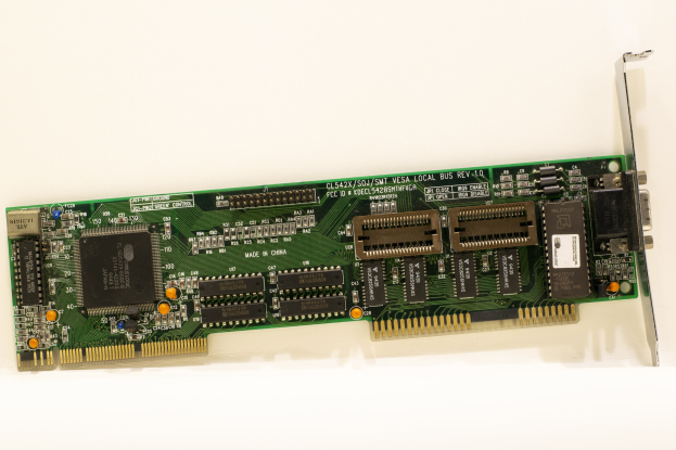 Nahaufnahme einer PCI-E-Karte mit einem zentralen Chip und mehreren angeschlossenen Verbindern auf einer weißen Oberfläche.