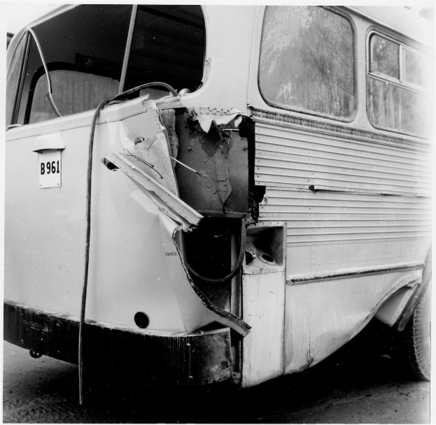 Schwarz-weiß-Foto eines Busses mit schwerer Frontschaden durch einen Autounfall, der auf der Straße positioniert ist.