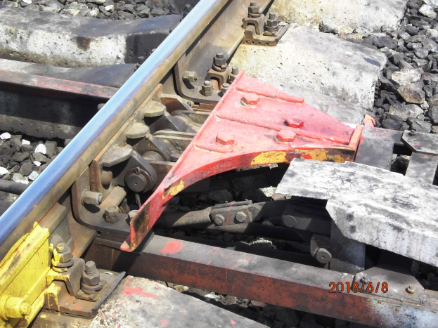 Nahaufnahme einer Schienenstrecke mit einer Metallschutzvorrichtung und Schottersteinen.