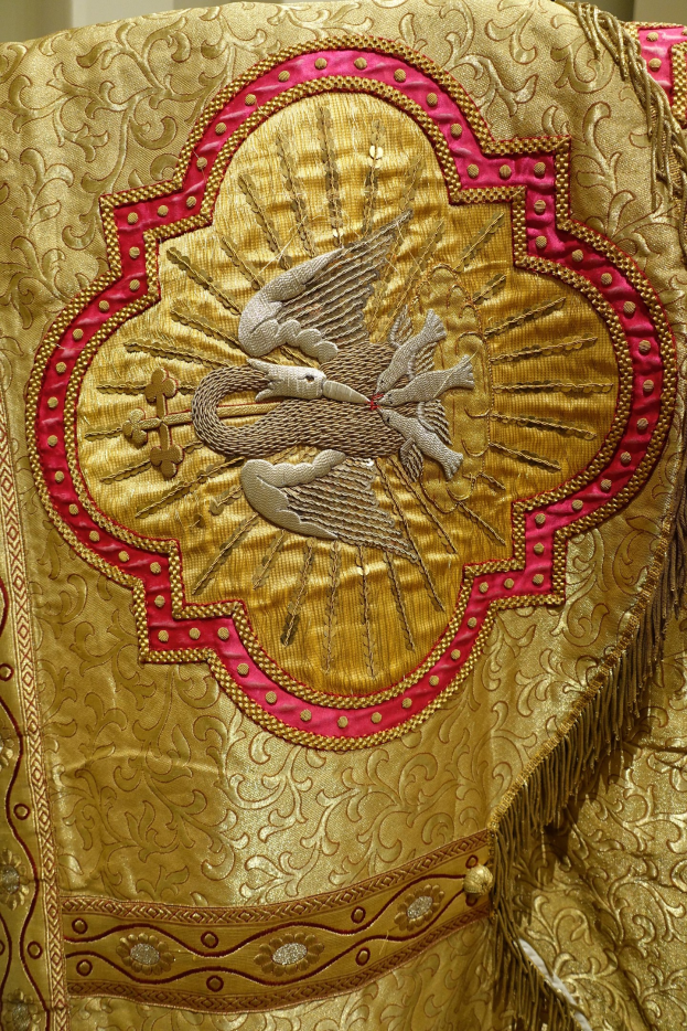 Nahaufnahme eines Priestergewandes mit aufwendiger Gold- und Rotstickerei vor einer Wand im Hintergrund