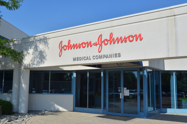 Außenansicht des Johnson & Johnson Medical Companies-Gebäudes mit Glaswänden und -türen, Text an der Wand, Steinen, Pflanzen und einem Baum auf der linken Seite unter einem klaren blauen Himmel.