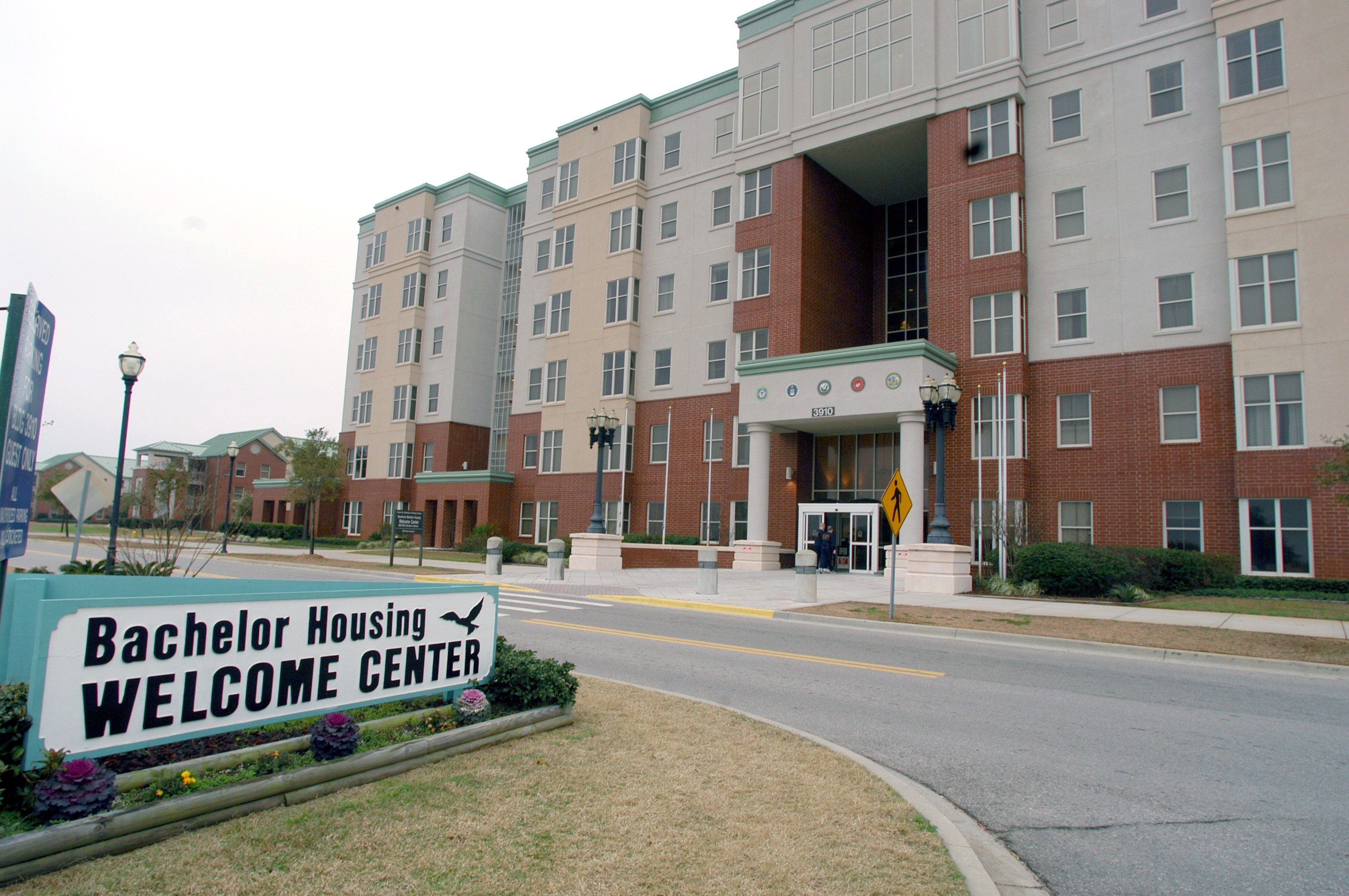 Ein Willkommenszentrum für Bachelor-Wohnungen mit Gebäuden, Straßenlaternen, Lampen, Schildern, Fahrzeugen, Grünflächen und einem klaren Himmel.