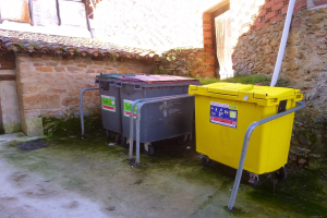 Zwei gelbe und graue Mülltonnen mit Rädern nebeneinander vor einem Gebäude mit einer Wand und einem Fenster im Hintergrund.