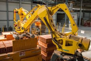 Großes industrielles Lager mit gestapelten Kisten, Kränen, Zäunen, Pfählen und einer fernen Wand in einer Manufacturing-Umgebung.