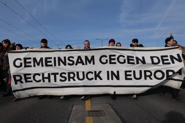 Eine Gruppe von Menschen mit einem Banner "Gemeinsam gegen den Rechtsruck in Europa" bei einer Protestaktion gegen die Europäische Union, mit Straßeninfrastruktur und Gebäuden im Hintergrund.