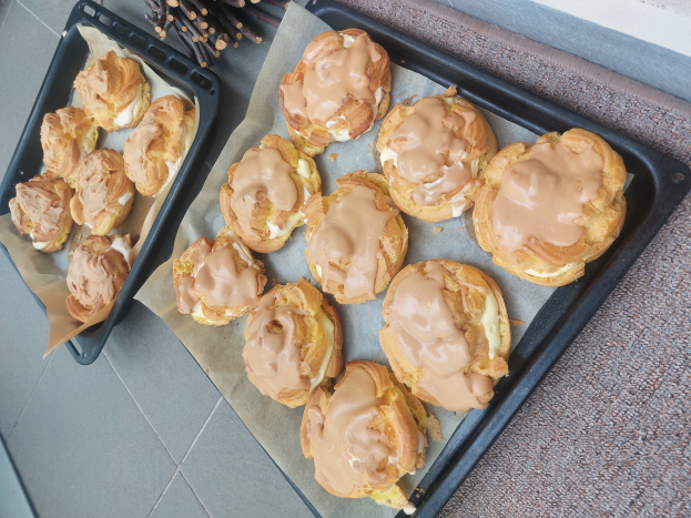 Ein Tablett mit verschiedenen dänischen Gebäckstücken, einige davon mit Puderzucker bestäubt, steht auf einer Theke neben einem offenen Fenster und wird von warmem Licht beschienen.
