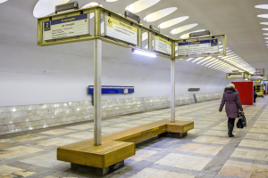 Eine Frau in einem Mantel mit einer Tasche geht durch eine Moskauer U-Bahn-Station mit Bänken, Texttafeln und Beleuchtung.