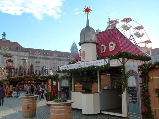 Ein geschäftiges Weihnachtsmarkt in Nürnberg, Deutschland, mit Menschen um geschmückte Stände, festliche Lichter und Schmuck, Gebäude im Hintergrund, einem Riesenrad und einer Tafel auf der rechten Seite.