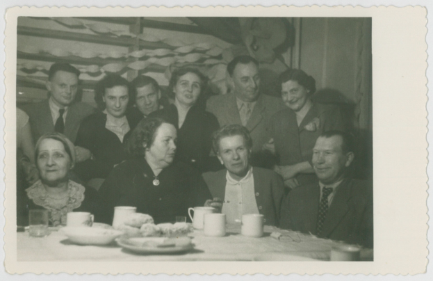 Eine Gruppe von Menschen sitzt um einen Tisch und teilt ein Mahl, lacht und genießt die Gesellschaft des anderen, mit Tassen, Untertassen, Tellern, Gläsern und Essen auf dem Tisch.