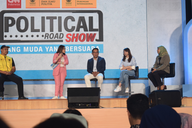 Eine Gruppe von Menschen sitzt auf einer Bühne mit einer Frau, die ein Mikrofon in der Mitte hält, einem Publikum im Vordergrund und einem Banner mit der Aufschrift "Politischer Straßenkampf 2019" im Hintergrund.