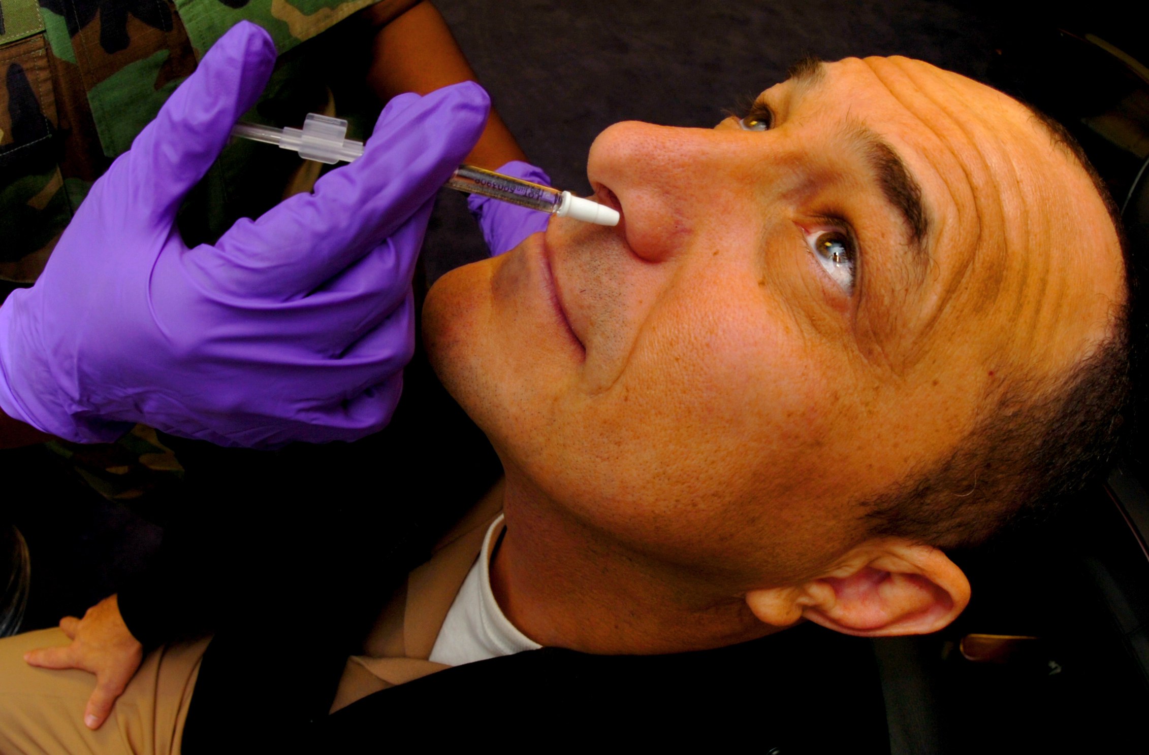 Ein Arzt in lila Handschuhen verabreicht einem Mann ein Vakzin mit einer Spritze.