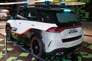 Mercedes-Benz E-Klasse Electric SUV auf der IAA in Frankfurt zu sehen, umgeben von Absperrpollern mit Seilen und Lichtern, mit einem weiteren Fahrzeug und einer textbedruckten Wand im Hintergrund.