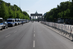 Lange Reihe von Polizeiwagen auf der Straße vor dem Brandenburger Tor geparkt, mit Fahrradfahrern und Fußgängern, Barrieren, Bäumen, einem Bogen mit Statuen im Hintergrund und sichtbarem Himmel.