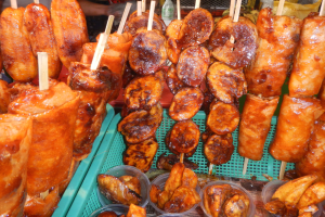 Marktstand mit Spießen von Hähnchenflügeln und verschiedenen Lebensmitteln in Plastikbehältern im Hintergrund.