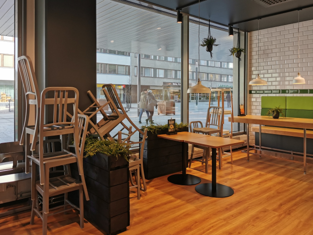 Ein Restaurant-Innenraum mit hölzernen Tischen und Stühlen, betrachtet durch ein großes Fenster, das eine Berliner Straßenszene mit Passanten, Gebäuden und urbanen Elementen zeigt.