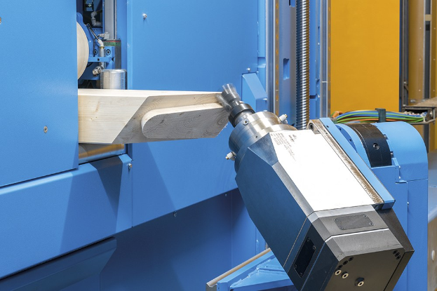 CNC-Fräsmaschine schneidet ein Holzstück in einer industriellen Umgebung mit sichtbaren Kabeln und einer Wand im Hintergrund.