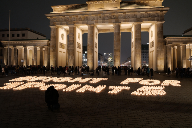 Eine Gruppe von Menschen steht vor dem beleuchteten Brandenburger Tor in Berlin, Deutschland, umgeben von Geb├Ąuden, Masten und Lichtern; die Worte "K├Ąmpfe für die Freiheit" sind im Vordergrund zu sehen.