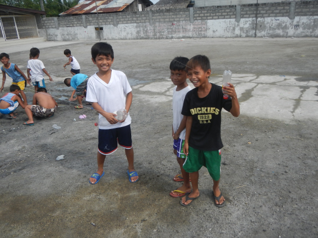 Junge Jungs, die in einer Parklücke stehen und Flaschen halten, mit Häusern, Bäumen und einem klaren Himmel im Hintergrund.