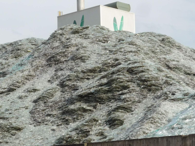 Ein großer Haufen aus Plastikmöll auf einer Zementwand mit einem Gebäude und einem klaren blauen Himmel im Hintergrund.