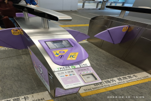 Eine Gruppe von Menschen vor einem Metalldetektor an einem Bahnhof, mit einem weiteren Metalldetektor rechts und einigen Menschen im Hintergrund.