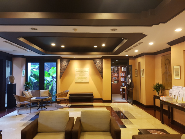 Eine Hotellobby mit Sofas, Stühlen, Tischen, Zimmerpflanzen, Büchern in Regalen, Deckenleuchten, Wandbehängen und Dekoration auf Beistelltischen, gefüllt mit natürlichem Licht von Fenstern und Türen.