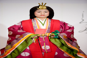 Eine Frau in einem traditionellen japanischen Kimono, das ein leuchtend rotes und grünes Kleid mit aufwändigen Mustern zeigt, steht selbstbewusst auf einem Laufsteg mit ihrem Haar zu einem ordentlichen Knoten gebunden.