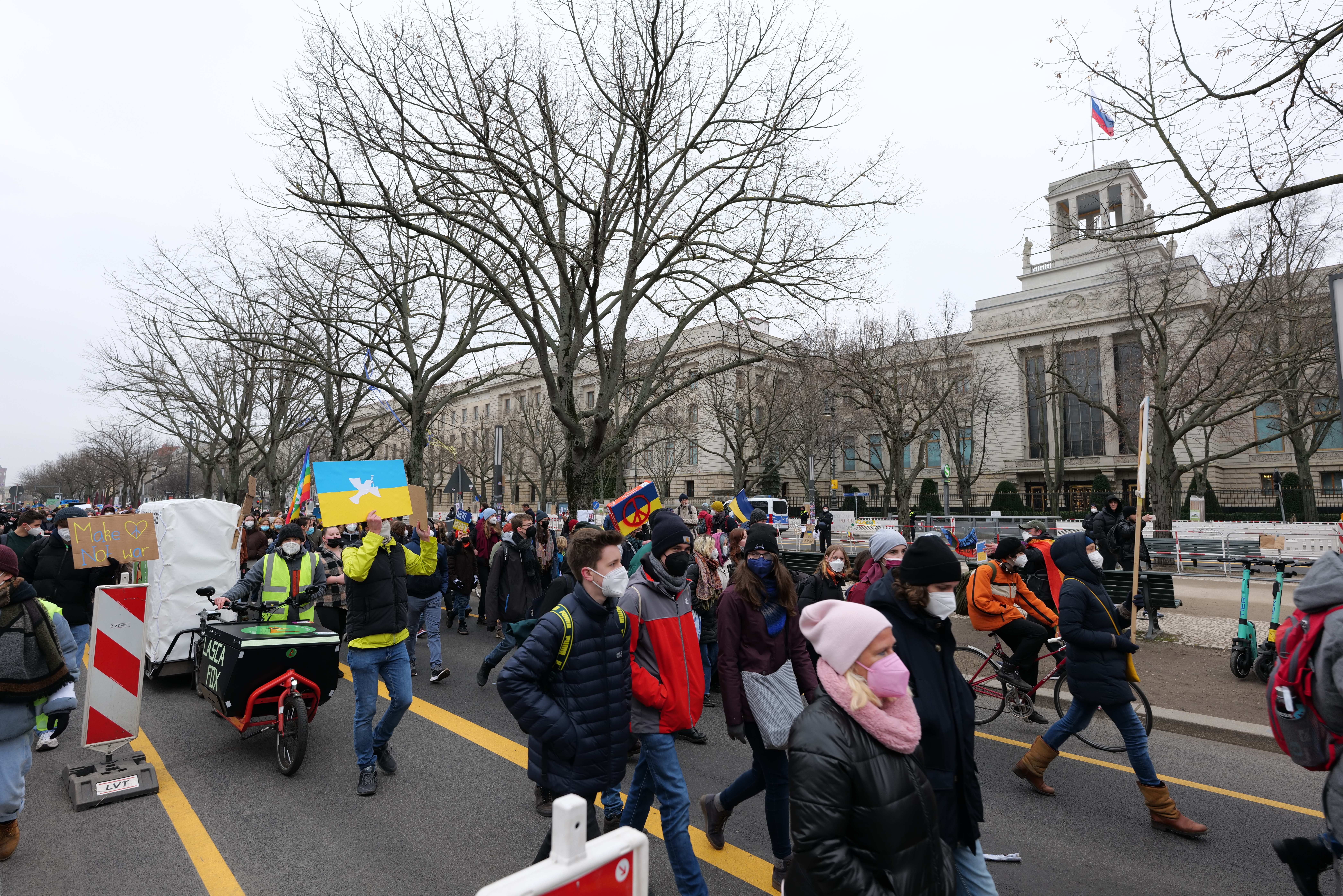 Eine große Gruppe von Menschen marschiert auf der Straße in Washington, D.C. am 21. Januar 2020 mit Schildern und Transparenten, während einige Fahrräder fahren, Schilderständer mit Stangen, Bäume und ein klarer blauer Himmel im Hintergrund.