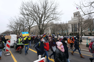 Eine große Gruppe von Menschen marschiert auf der Straße in Washington, D.C. am 21. Januar 2020 mit Schildern und Transparenten, während einige Fahrräder fahren, Schilderständer mit Stangen, Bäume und ein klarer blauer Himmel im Hintergrund.