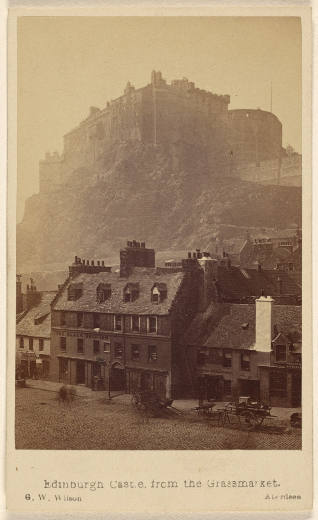 Alte Fotografie von Edinburgh Castle aus der Grassmarket-Sicht mit Gebäuden und Pferdewagen im Vordergrund und einem Hügel im Hintergrund; lesbarer Text am unteren Rand.