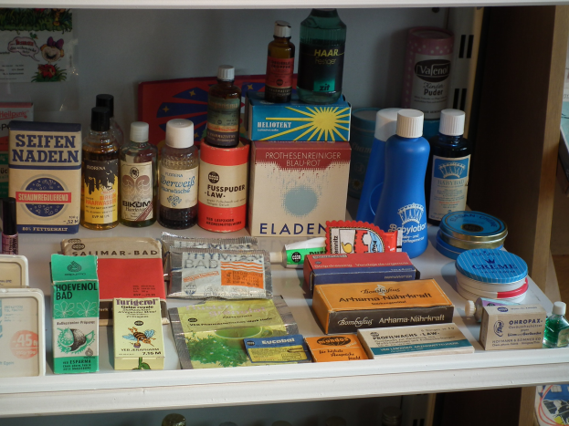 Ein Medizinschrank mit verschiedenen Flaschen, Schachteln und anderen Gegenständen sowie einem Regal mit zusätzlichen Vorräten.